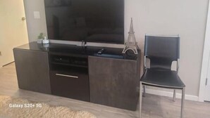 A modern living room with a large flat-screen TV mounted on a dark wooden cabinet, a small Eiffel Tower model, and a black chair.