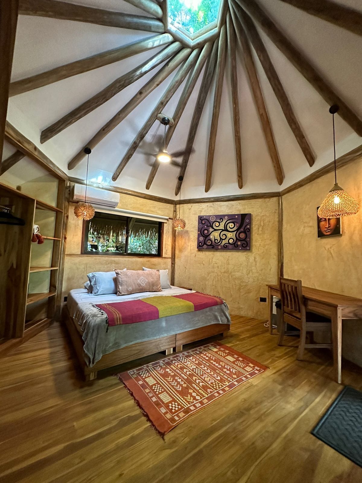 A cozy bedroom with a sloped ceiling, a bed with a colorful blanket, a wooden desk, and a chair.