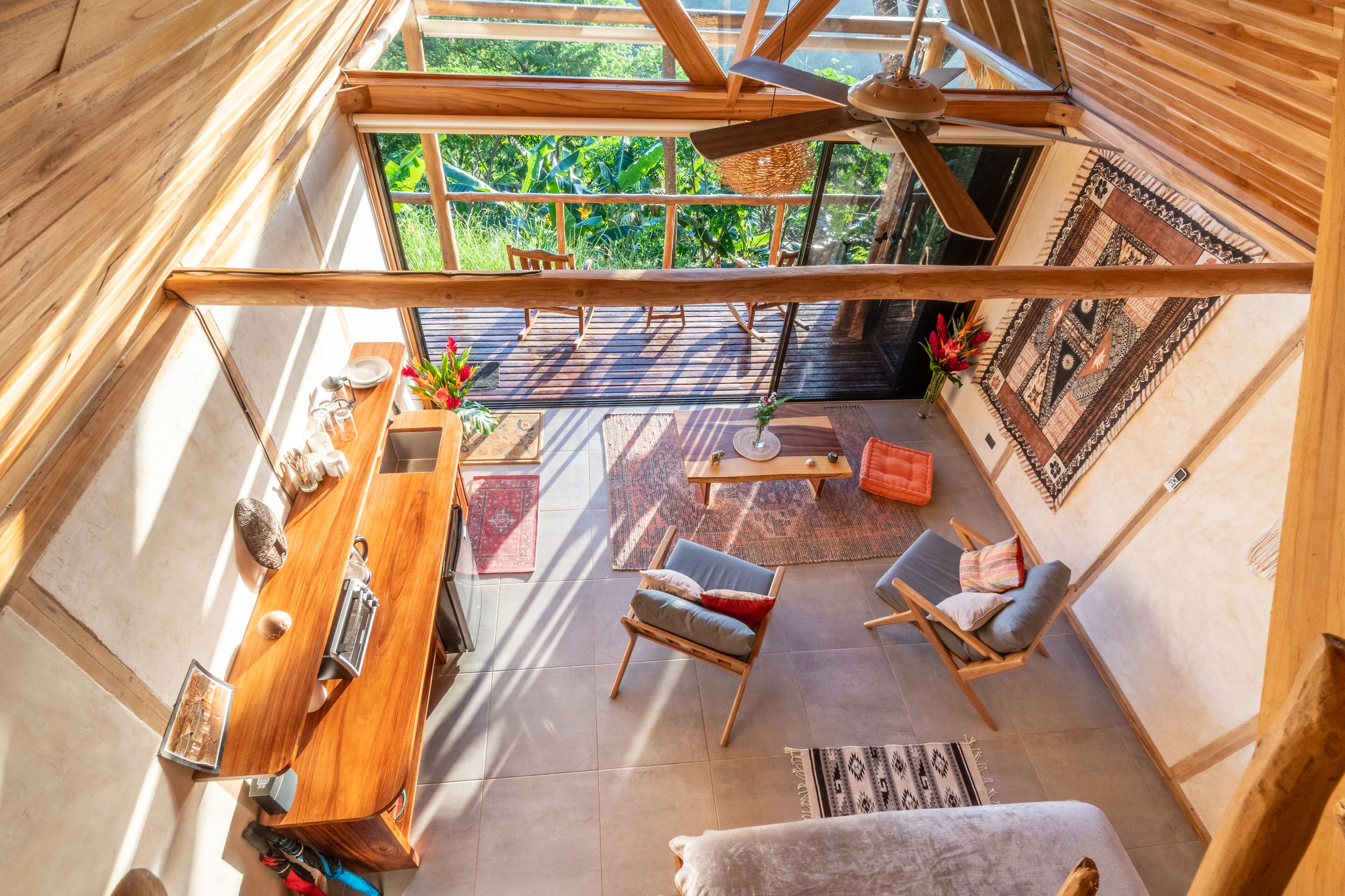 Amplio espacio tipo loft con techo alto, vigas de madera, un ventanal y vistas al verdor exterior.