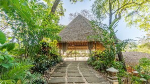 A thatched-roof hut with a stone pathway leading to it, surrounded by lush greenery. - Tierra Encantada Wellness Center (Nosara)