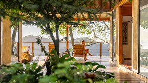 A wooden deck with a view of the sea, a person sitting on a chair, and a Buddha statue. - Tierra Encantada Wellness Center (Nosara)
