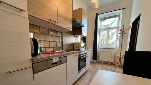 A modern kitchen with wooden cabinets, a built-in oven, and a window with a view of greenery. - EasyStay 3BR shared Apt. Near Meidling (Vienna)