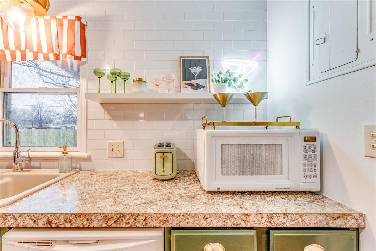 Une cuisine avec des carreaux de céramique blancs disposés en motif métro, un micro-ondes blanc, un grille-pain vert et une étagère ornée d’objets décoratifs.