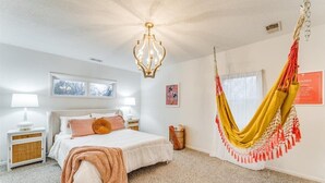 Un dormitorio con cama, lámparas de noche, una silla colgante y una ventana.