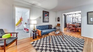 Una sala moderna con un sofá azul, una mesa de centro de madera y un tapete estampado. Hay un comedor con sillas y una mesa de madera.