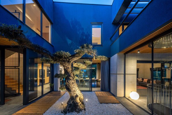Ein modernes Gebäude mit blauer Fassade, ein großer Baum in der Mitte und eine Glastür zu einem Innenraum.