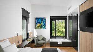 Un dormitorio moderno con una cama grande, un escritorio, una silla, un televisor y una ventana con vistas a árboles.