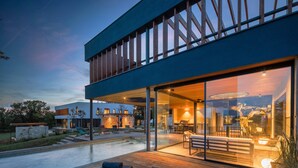 Una casa moderna de dos pisos con fachada de vidrio, mobiliario exterior y una piscina.