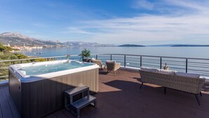 A deck with a hot tub, wicker furniture, and a view of a lake and mountains. - Beachfront Villa Atlantis with Pool (Kaštel Štafilić)