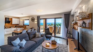 Ein modernes Wohnzimmer mit grauem Sofa, einem Couchtisch und einem Essbereich mit Meerblick.