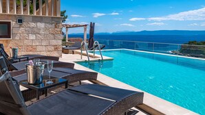 Ein Poolbereich mit Liegestühlen, einem Tisch mit Getränken und Blick auf das Meer.
