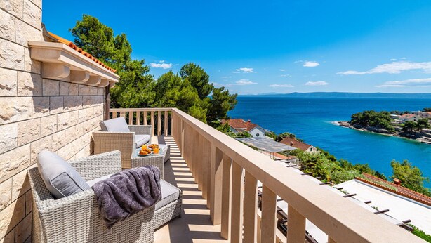 Ein Balkon mit Korbmöbeln, einem Tisch mit Speisen und Blick auf das Meer und die Küste.