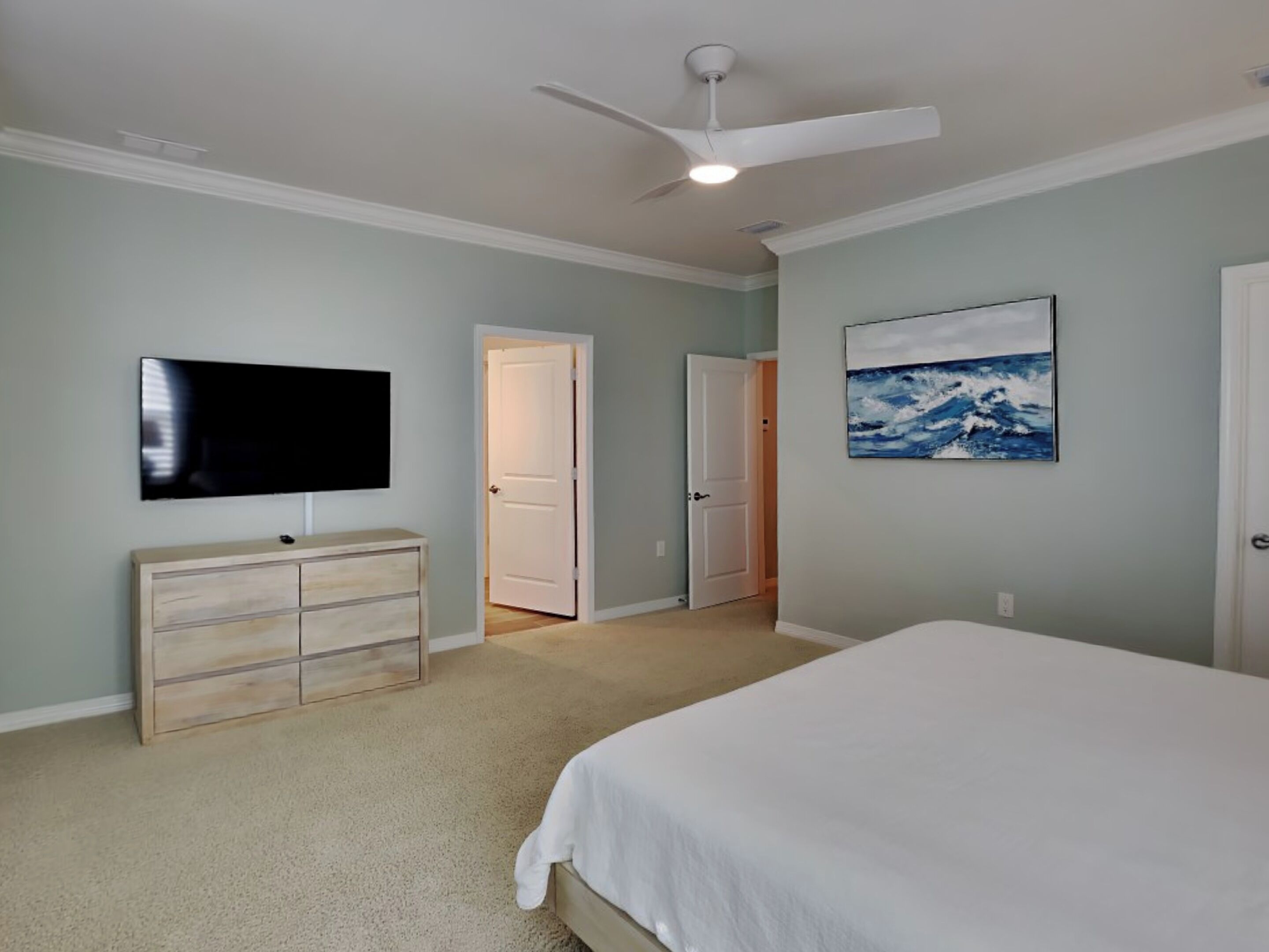 Ein Schlafzimmer mit Bett, Fernseher, Kommode, Deckenventilator und einem Bild an der Wand.