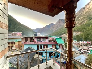 A view from a balcony overlooking a mountainous village with buildings and a clear sky. - Diamond Valley x One Light Stays (Bhuntar)