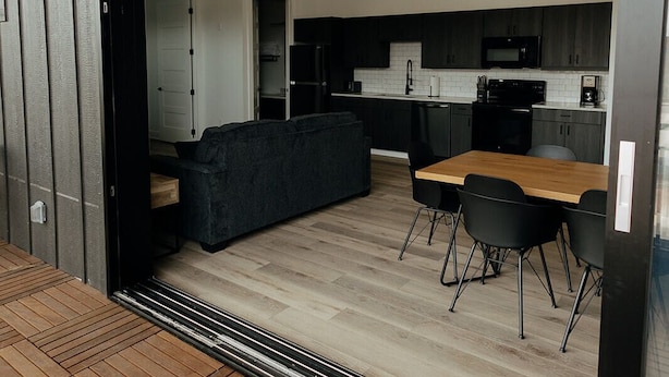 Eine moderne Küche mit dunklen Schränken, einem Holzes Esstisch und einem schwarzen Sofa.