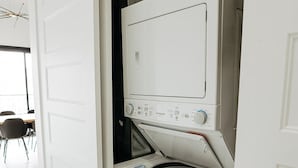 Eine kompakte, weiße Waschmaschine und Trockner in einem, eingebaut in einem schmalen Raum, vermutlich einem Hauswirtschaftsraum oder einer Waschküche.