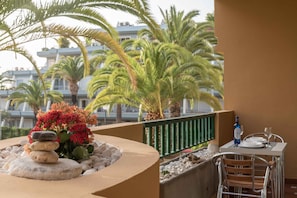 A balcony with a table set for dining, a decorative rock arrangement, and a view of palm trees and a building in the background.