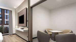 A modern hotel room with a flat-screen TV mounted on a wall, a small table, two sofas, and a large window offering a view of the city. - Days Inn by Wyndham Yangzhou Guangling (Yangzhou)