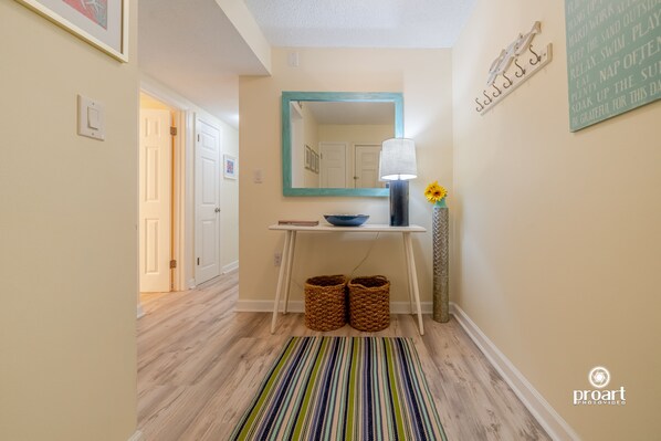 A hallway with a striped rug, a mirror, a table with a bowl, and baskets. - Hello Sunshine, 60 yards from the beach (Destin)