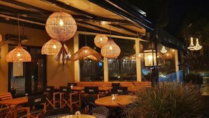 An outdoor seating area with wicker lampshades and wooden tables and chairs. - Hotel Liberté (Schoorl)