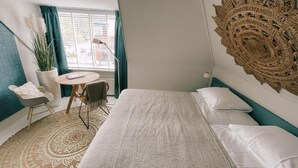 A bedroom with a bed, a round table, a chair, a potted plant, and a decorative wall piece. - Hotel Liberté (Schoorl)