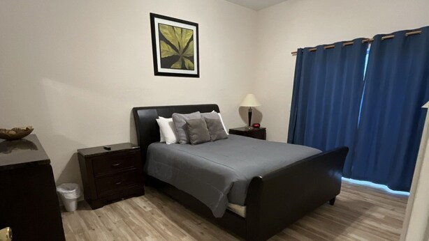 Une chambre à coucher avec un lit, une table de chevet, une lampe, une poubelle et un tableau au mur.