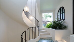 A spiral staircase with black railings and patterned floor tiles, leading to a landing with a window and a potted plant. - Las Catalinas- Spectacular views- breakfast service, Casa Chameleon's neighbor (Las Catalinas)