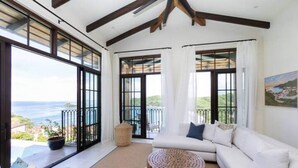 A spacious living area with a large window overlooking a scenic view, a white sofa, and a round wooden coffee table. - Las Catalinas- Spectacular views- breakfast service, Casa Chameleon's neighbor (Las Catalinas)