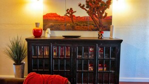 Un salon comprenant une bibliothèque, un tableau représentant un paysage désertique et deux lampes fixées au mur.