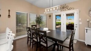 Un comedor con una mesa y sillas de madera oscura, un jarrón blanco y vistas al exterior a través de la puerta.