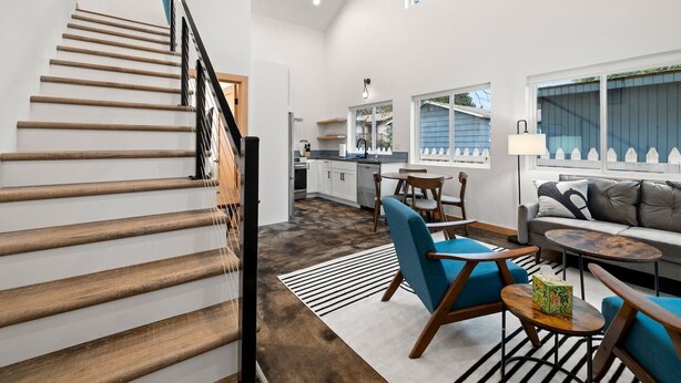 Ein modernes Interieur mit einer Holztreppe, einer Küche, einem Essbereich und einem Wohnzimmer mit Sofa und Couchtisch.