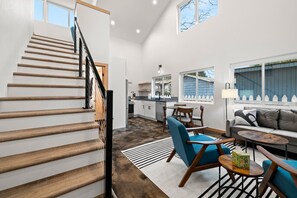 Un intérieur moderne comprenant un escalier en bois, une cuisine, un coin repas et un salon avec un canapé et une table basse.