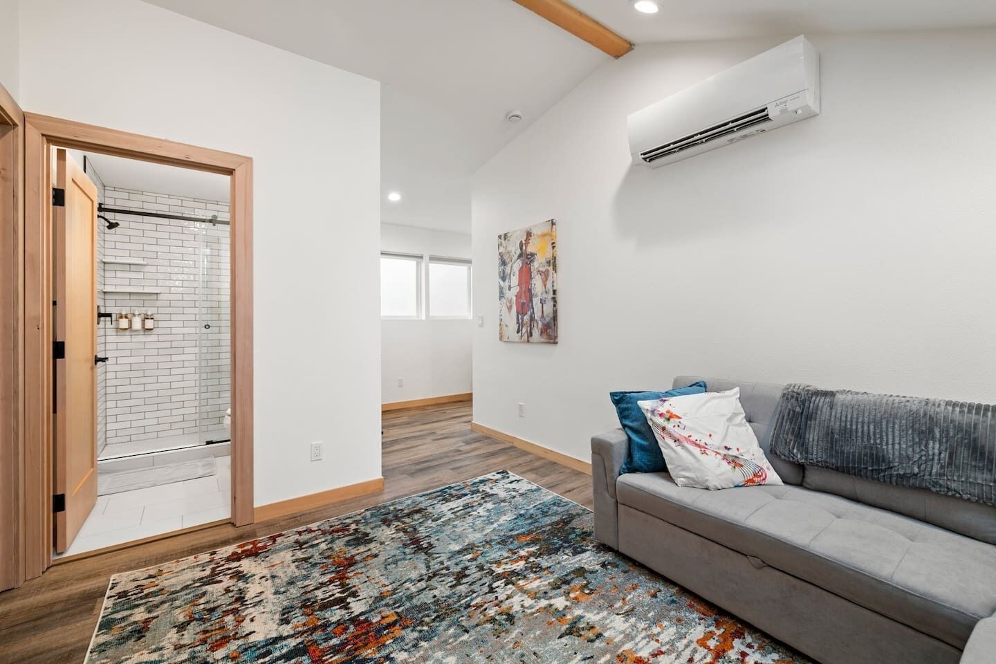 Un salon moderne avec un canapé gris, un tapis coloré et un tableau accroché au mur.