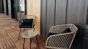 Un espacio al aire libre techado con dos sillas de mimbre, suelo de madera y un ventanal grande.