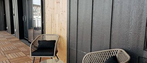 A covered outdoor area with two wicker chairs, a wooden floor, and a large window.