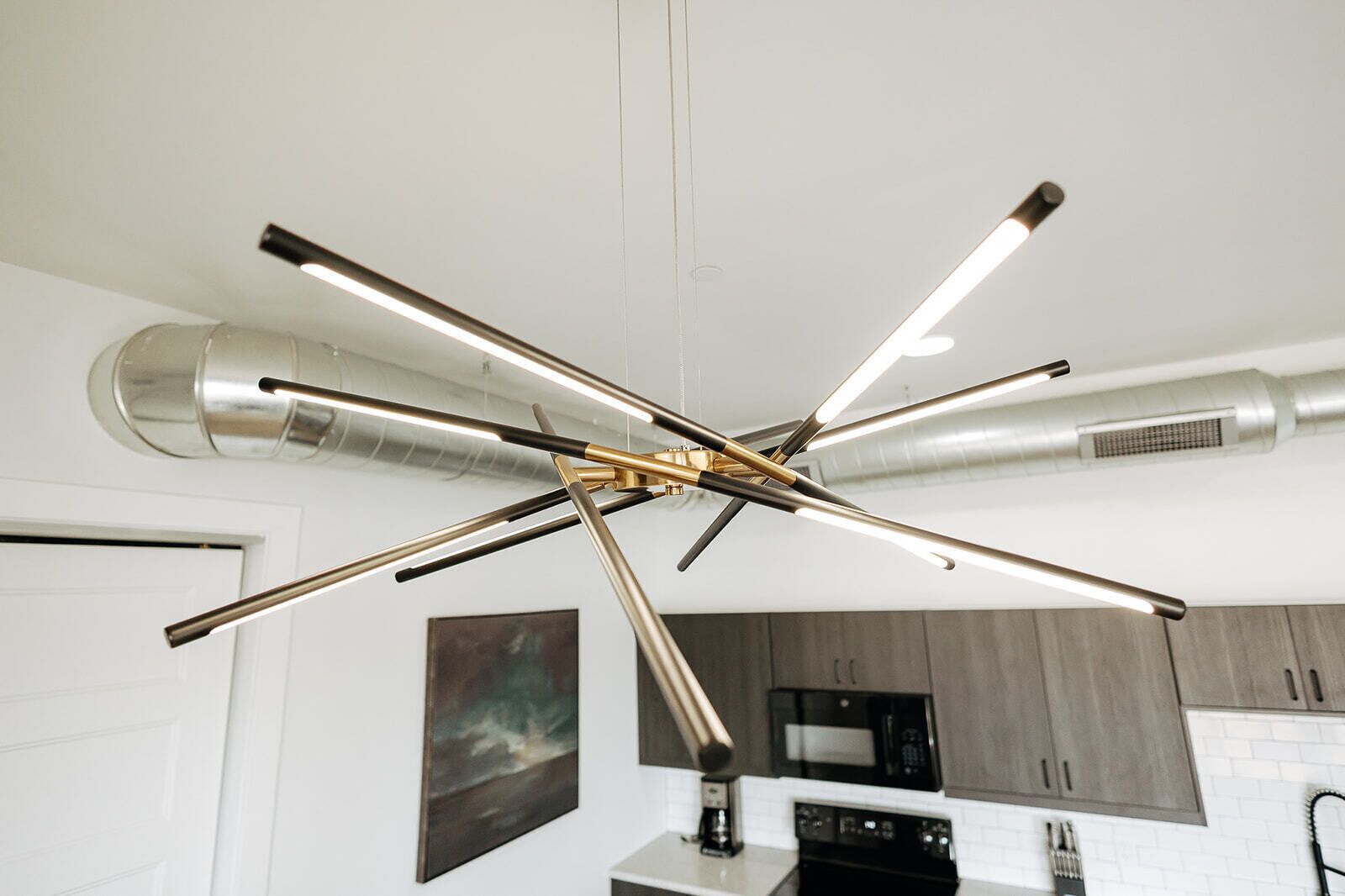 Uma cozinha moderna com luminária de teto diferenciada, paredes brancas e armários de madeira.