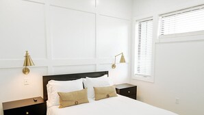 Un dormitorio con cama, mesitas de noche, ventilador de techo y ventana con persianas.