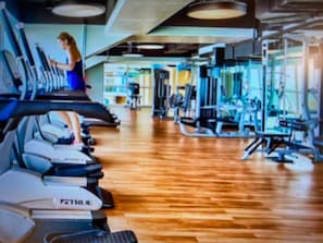 A gym with treadmills, weight machines, and a wooden floor.