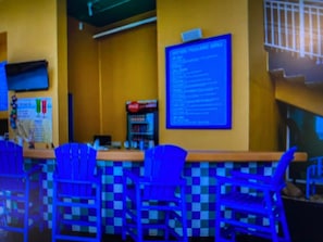 A bar area with blue checkered chairs, a counter, and a menu board.
