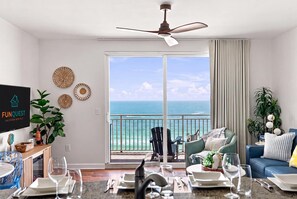 A room with a dining area, a television, a ceiling fan, a view of the ocean, and a balcony with chairs. - Splash 804E (Panama City Beach)