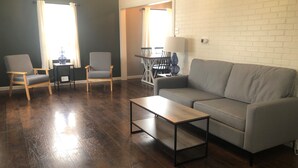 Un salon avec un canapé gris, deux fauteuils, une table basse et une table à manger avec des chaises.