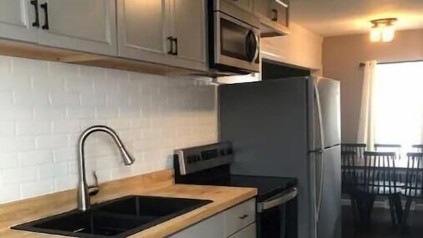 Une cuisine moderne avec des armoires blanches, un plan de travail en bois, un four à micro-ondes, une cuisinière et un réfrigérateur.