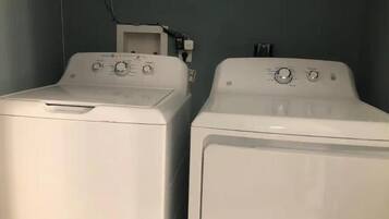 Two white front-loading washing machines in a laundry room with a plain wall and a power outlet visible.