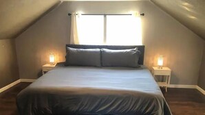 Une chambre à coucher avec un grand lit, deux tables de chevet avec des lampes et une fenêtre avec des rideaux.