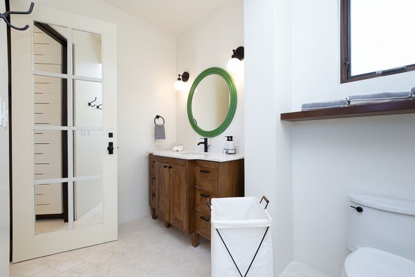 A bathroom with a wooden vanity, a green-framed mirror, and a white toilet.