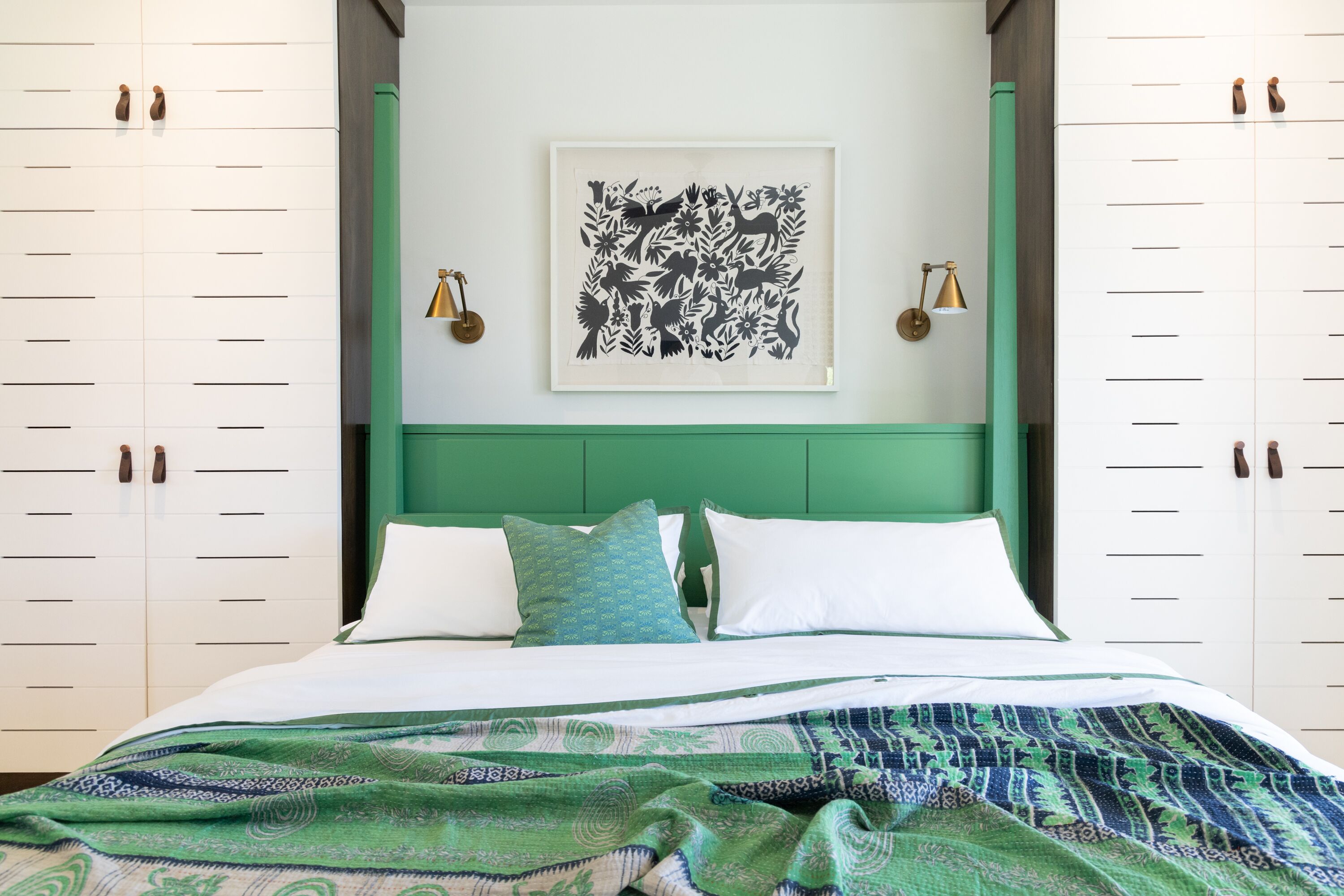 Une chambre à coucher avec un lit, une tête de lit verte, des murs blancs et une œuvre d’art encadrée au-dessus du lit.