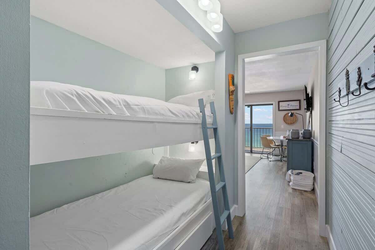 A bunk bed room with a ladder, a desk with a chair, and a view of the sea.