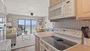 Cocina moderna con microondas, estufa y horno integrados.  Comedor con mesa y sillas, y vista al océano a través de amplios ventanales.