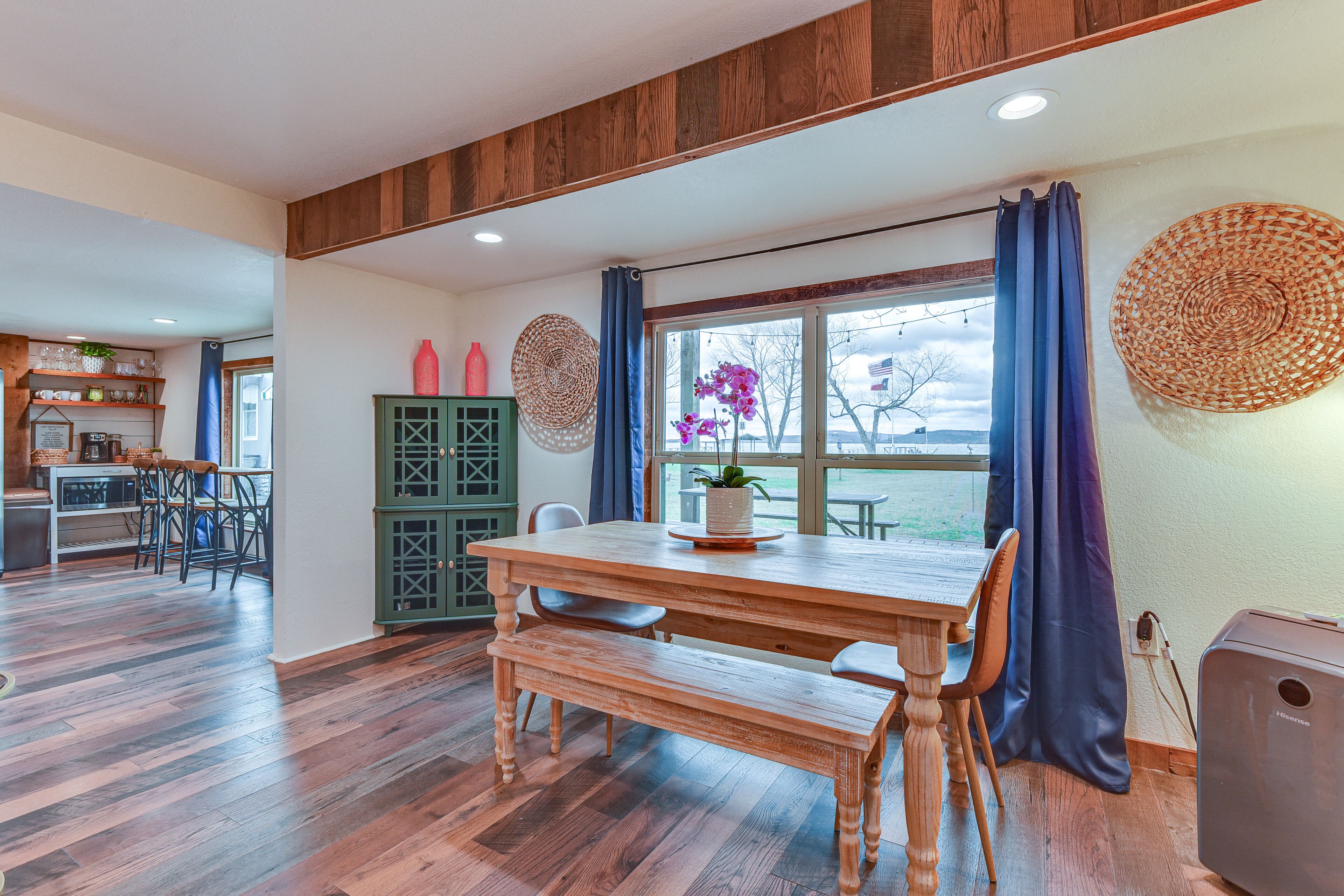 Un coin repas avec une table et des bancs en bois, un buffet vert et une vue par une fenêtre ornée de rideaux.