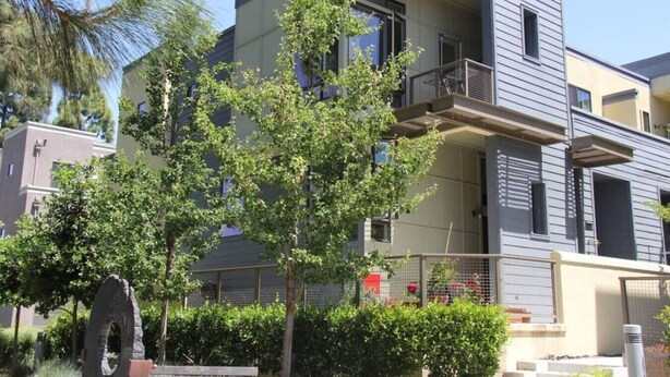Un edificio moderno de varios pisos con balcones, rodeado de vegetación y un arco de piedra.